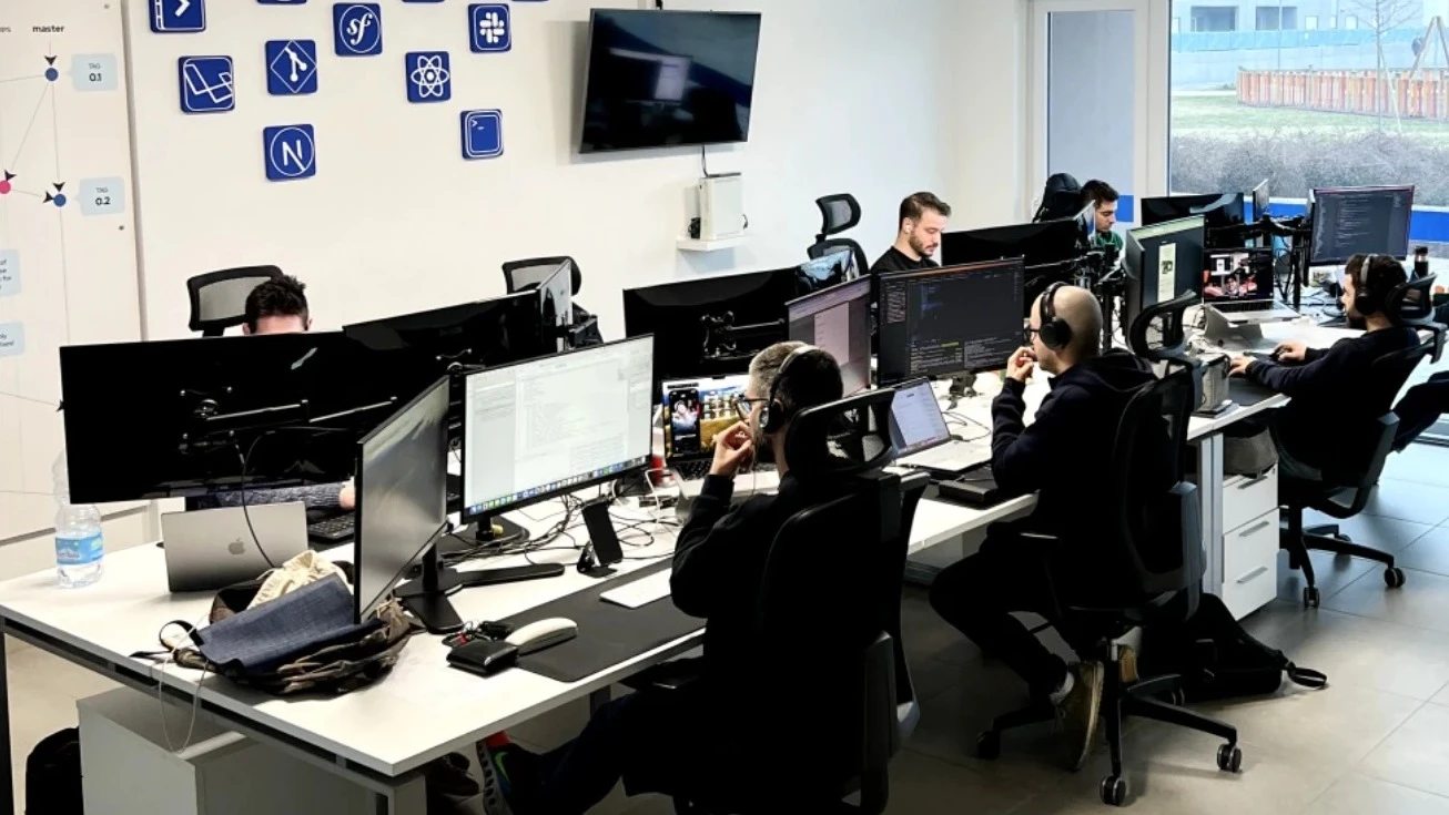 L’open space di dotenv: sette persone al lavoro davanti ai monitor, e sul muro le icone degli strumenti che usiamo